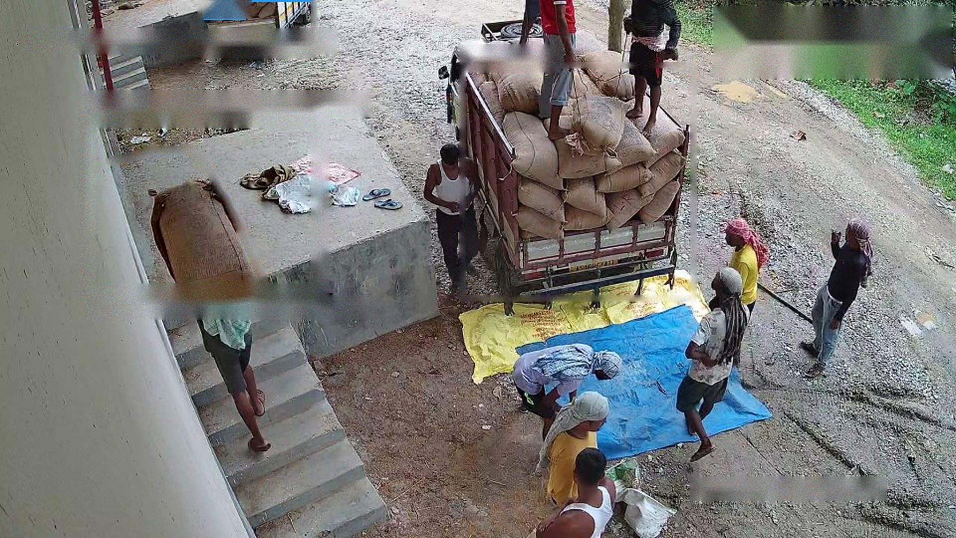 Live industrial CCTV view of a truck being unloaded at a warehouse loading bay, with workers carrying bags